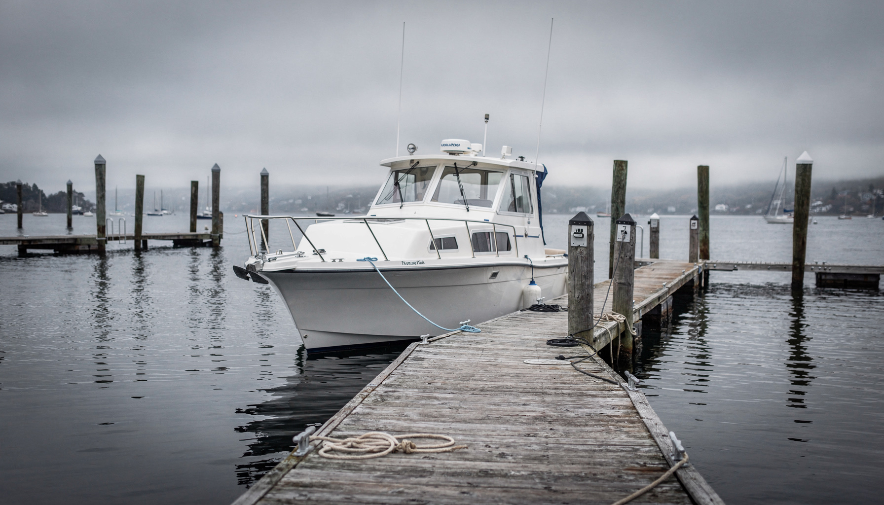 A single cabin cruiser tied up alone at a quiet brokerage dock, the kind of used boat a survey is used to price and negotiate.