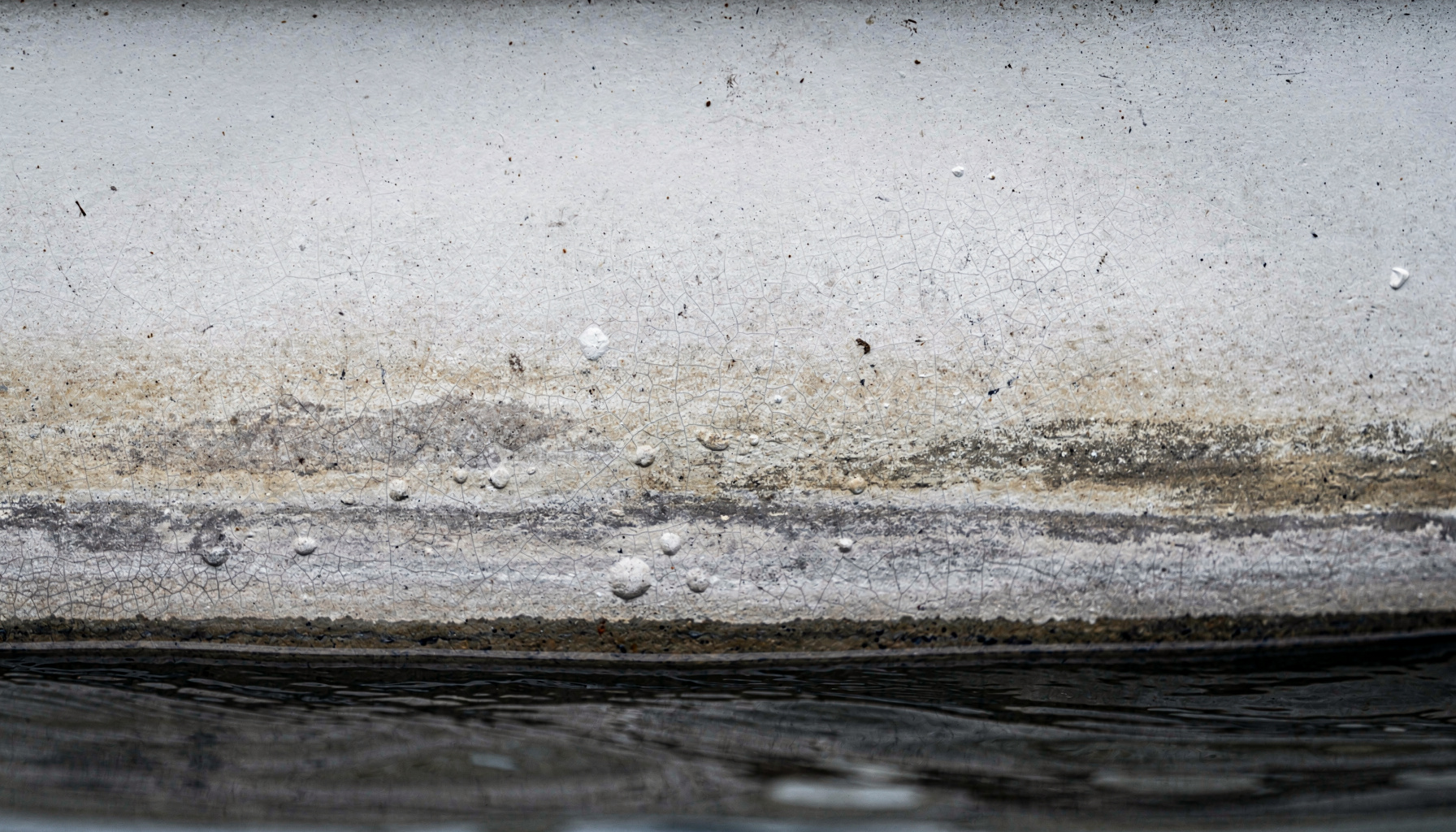 A close-up of a weathered fiberglass hull near the waterline showing faded gelcoat and small blisters, the kind of wear a survey flags.