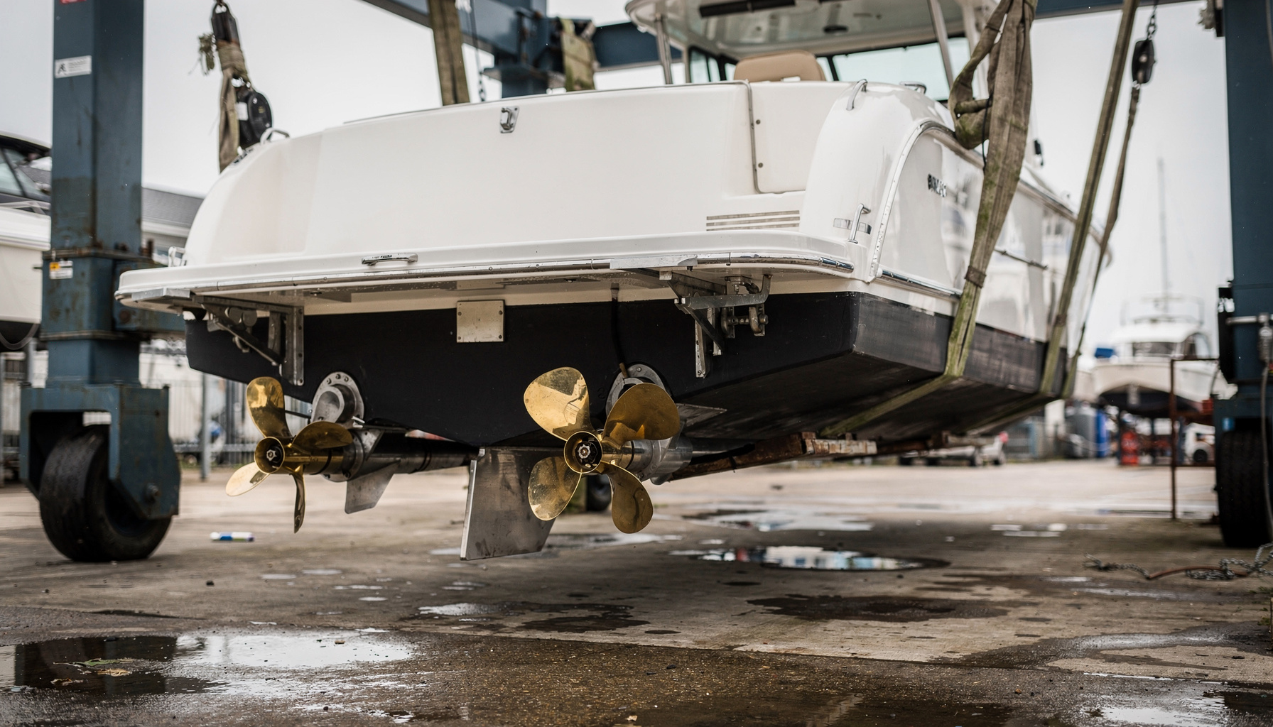 A powerboat raised in a travel-lift with its propellers, shafts, and rudder exposed, the running gear a pre-purchase survey inspects